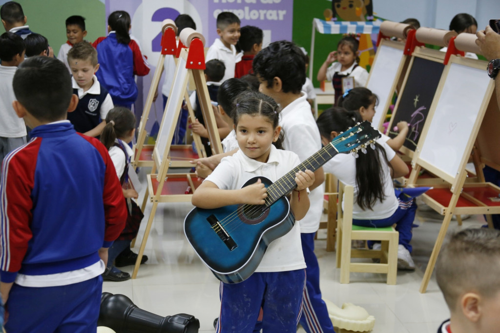 Niño con guitarra en mano, al fondo más niños dibujando en caballetes